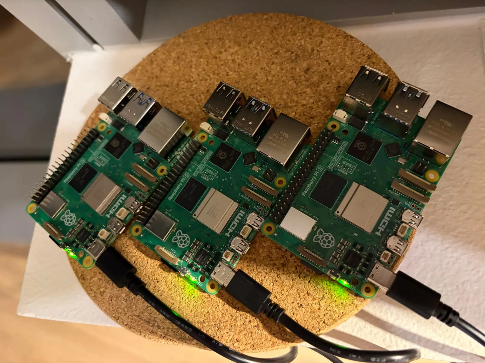 Three Raspberry Pi 5 boards side by side on a cork mat, powered over USB-C with green activity lights on