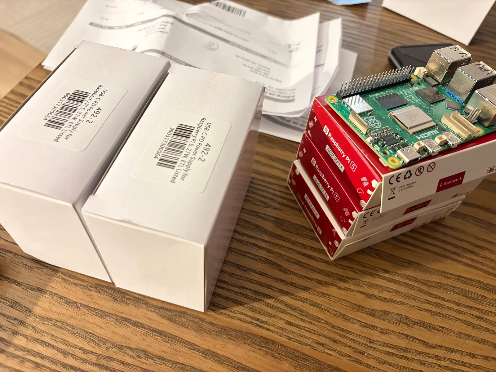 Three Raspberry Pi 5 4GB boxes stacked next to two boxed USB-C power supplies, with one board unboxed on top